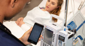 medical worker using phone to check equipment by patient's bed